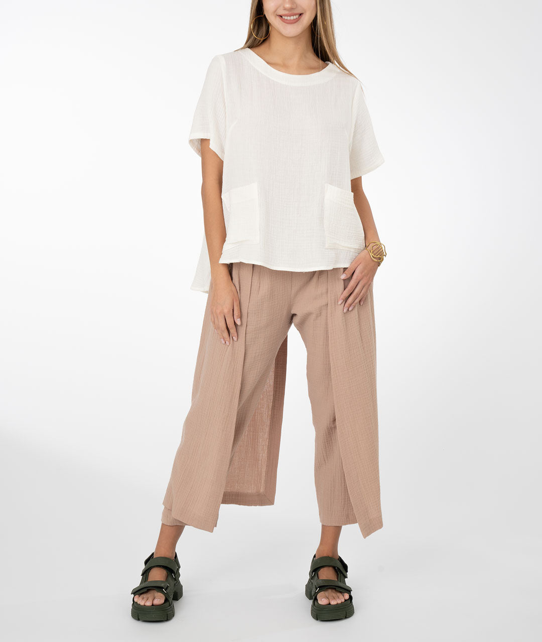 model in a khaki color pant with draped panels on either side, worn with a white boxy top with bust darts, square hip pockets and a slightly lower back