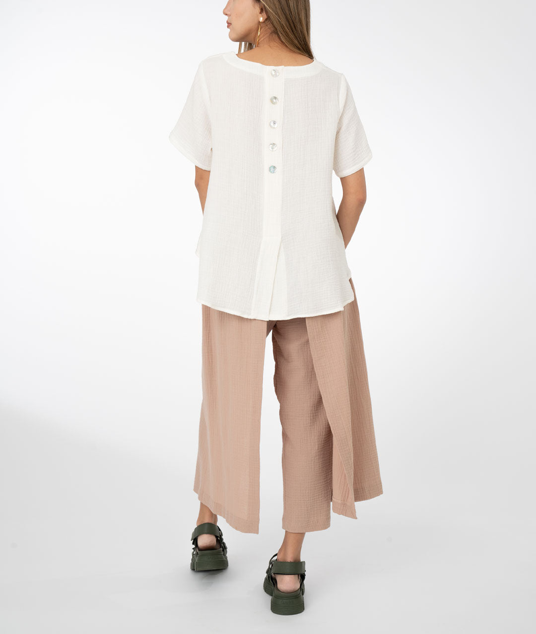 model in a khaki color pant with draped panels on either side, worn with a white boxy top with bust darts, square hip pockets and a slightly lower back