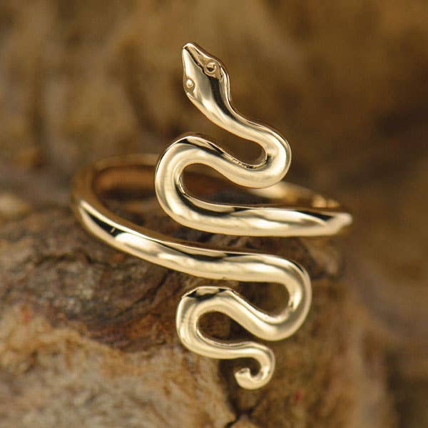 Close up of coiled snake ring in bronze. Ring is open in the center. Against a dark caramel texture background 