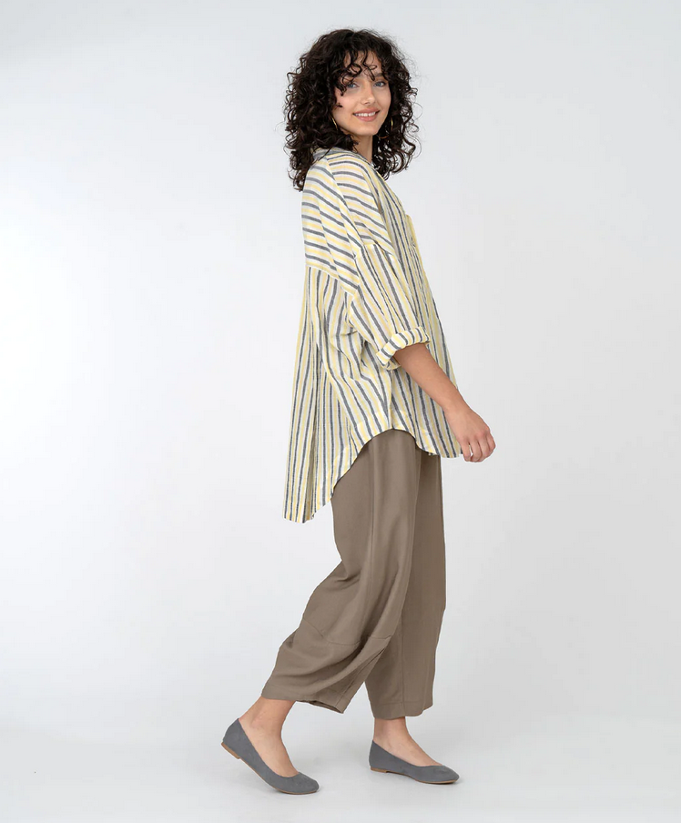 side view of brunette model wearing yellow and black stripe top and khkai pants with bubble hem. On a white background.