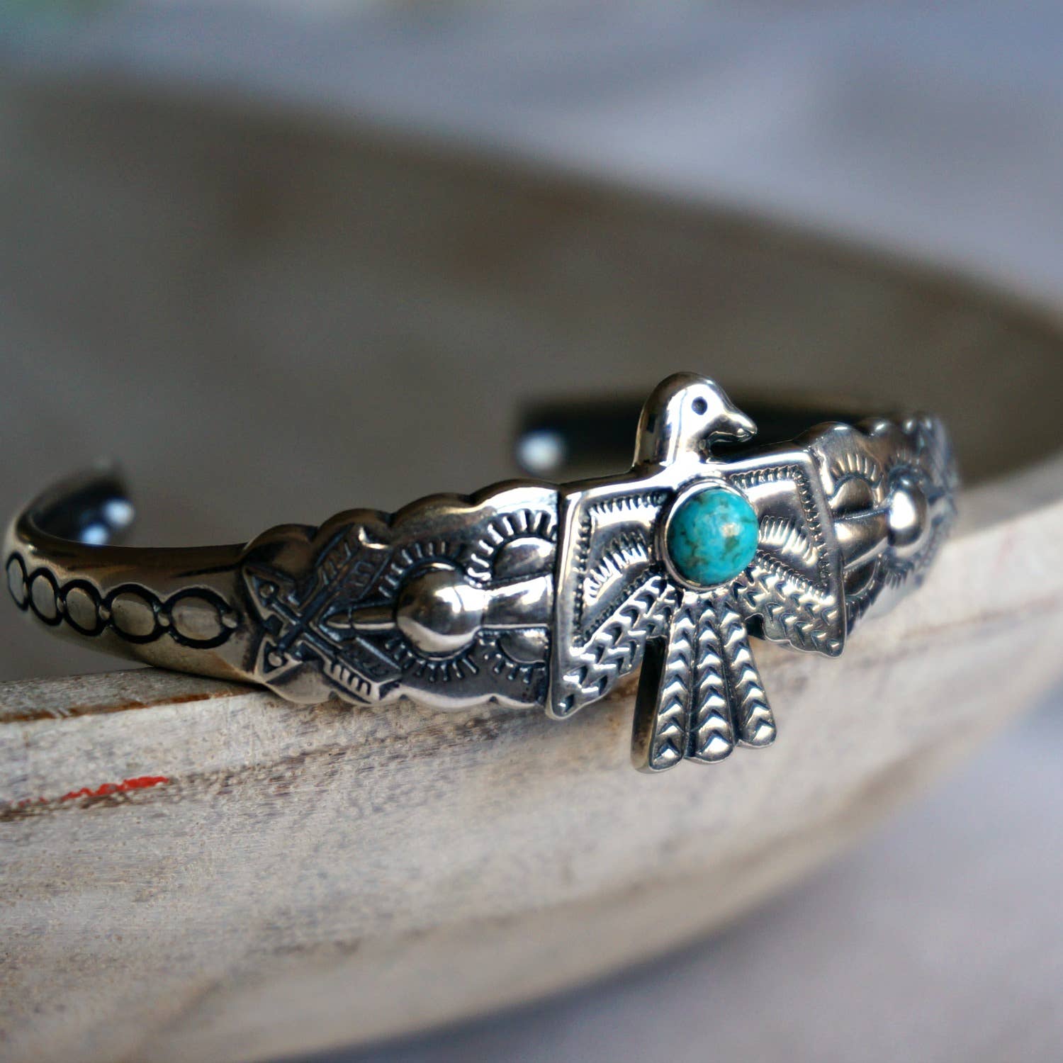 Slim detailed Sterling silver cuff w/ Thunderbird design and one Turquoise stone inlay set against a grey background