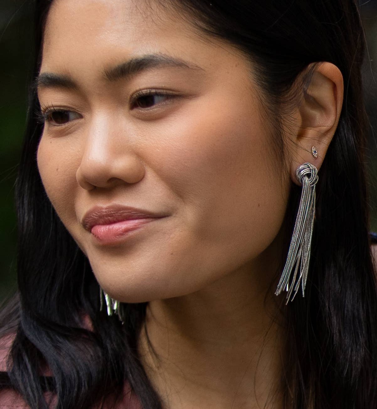 Close up of brunette model wearing gold earrings with knot and long dangling cluster of chains