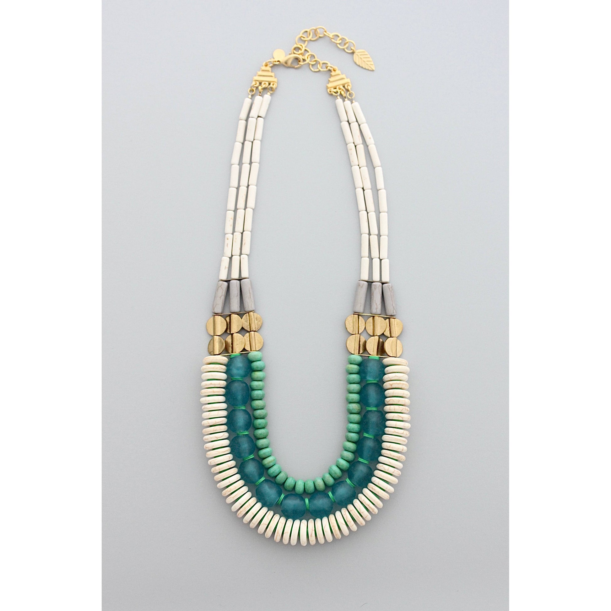 20" triple strand necklace with magnesite, turquoise, vinyl, brass, and Ghana glass against a grey background