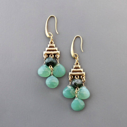 Close up of gold tone earring with hook,, stack of three pyramid gold bars, and 4 stones dangling below, 3 light teradrops in aqua and one round dark grey. Against a light grey background.