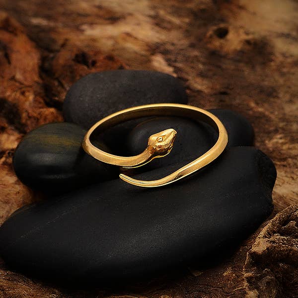 close up of bronze ring in the shape of a snake in a single circle. Set on 4 black stones, against a dark textured background on a dark caramel color