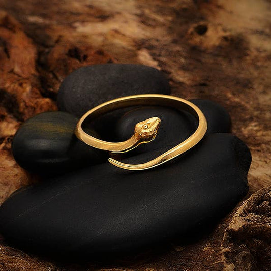 close up of bronze ring in the shape of a snake in a single circle. Set on 4 black stones, against a dark textured background on a dark caramel color