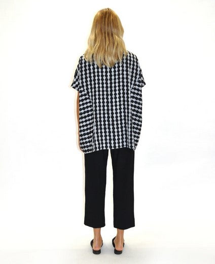 Back view of blond model with wearing black anhle length pants and a black and white polka dot stripe print loose top and black point flat mules. Against a white background