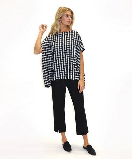 model with one arm up wearing black anhle length pants and a black and white polka dot stripe print loose top and black point flat mules. Against a white background