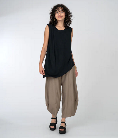 Sleeveless top with beautiful gather at one shoulder and asymmetrical hemline. Taupe pants and black platform sandals.,