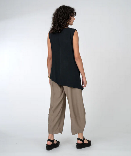 back view of Sleeveless top with beautiful gather at one shoulder and asymmetrical hemline. Taupe pants and black platform sandals.,
