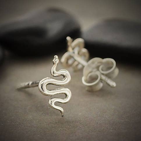close up of coiled silver snake post earrings. One earing is shown in the front in full focus, other is shown out of focus from the back with earring back. Two black pebbles in the background. Against a grey ground.