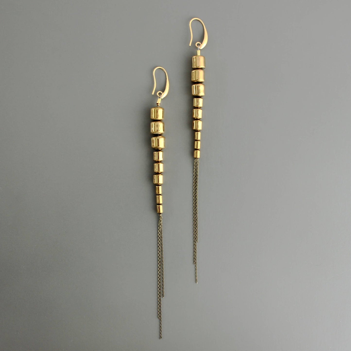 Super long shiny earrings are a 70s Studio 54 vibe. 18k gold plated brass hooks with 9  plated hematite beads and brass chain. 6.5 inches from top of hook to bottom of chain. Against a grey background