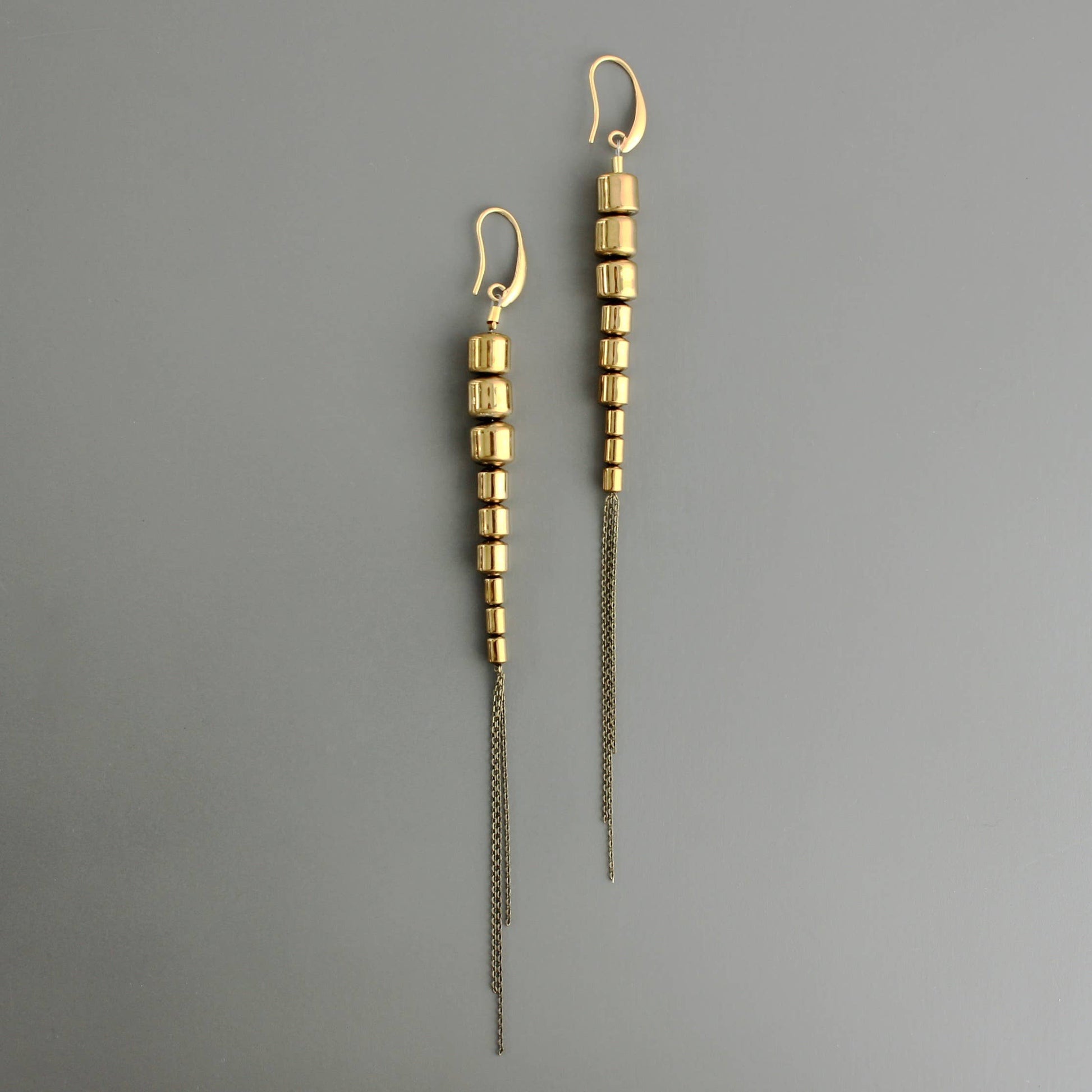 Super long shiny earrings are a 70s Studio 54 vibe. 18k gold plated brass hooks with 9  plated hematite beads and brass chain. 6.5 inches from top of hook to bottom of chain. Against a grey background
