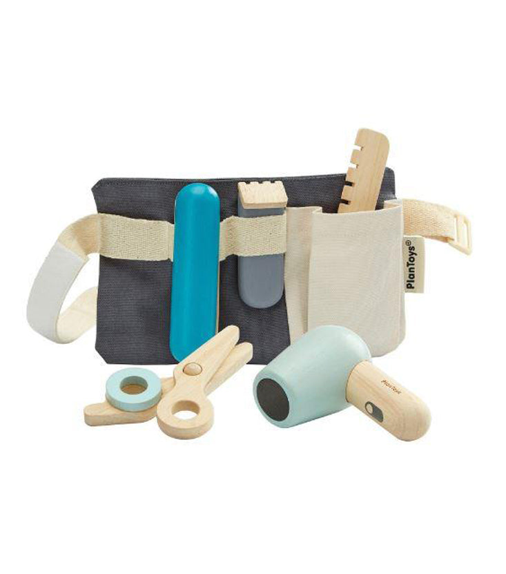 Play hairdresser set that includes a navy blue utility belt. On the belt, there is are several wooden toys: a blue hair straightener, clippers, wooden comb, wooden scissors, and a baby blue blow dryer. Pictured against a white background.
