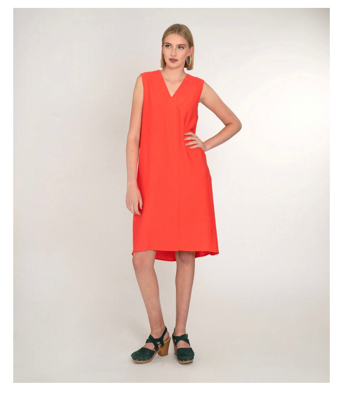 model in a sleeveless vneck coral dress, in front of a white background