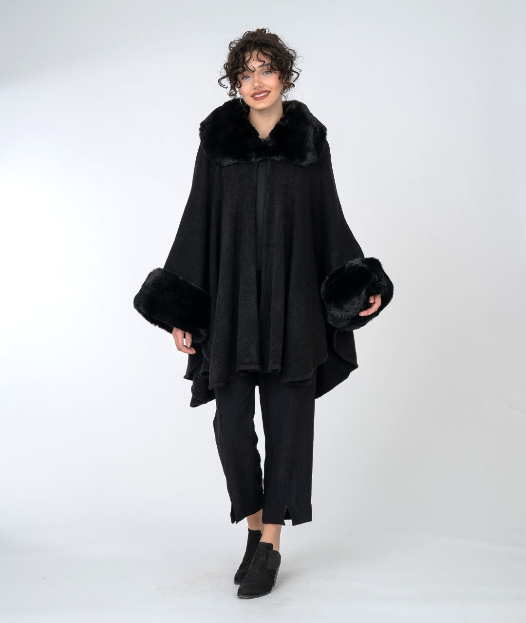 model is wearing all black with a black, fur trimmed cape over top