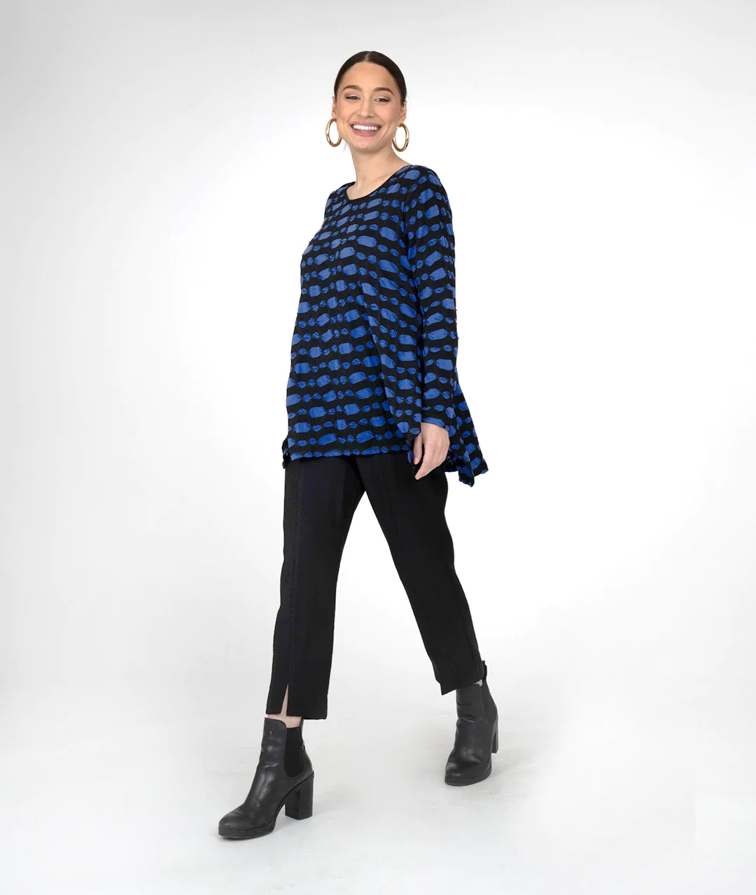 modelwearing blue and black round nwck top and black pants and boots and hoop earrings. on a white background. 