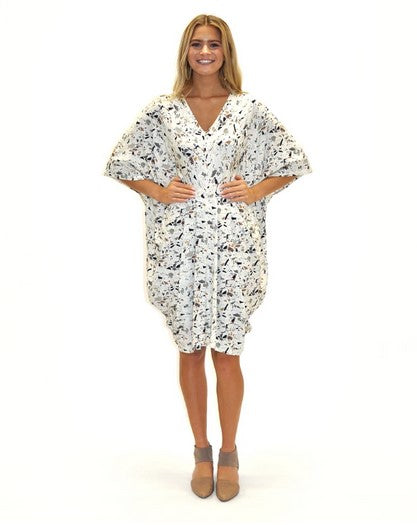 blond model wearing a v-neck kaftan style dress in a white terrazzo print and taupe shoes. Against a White background