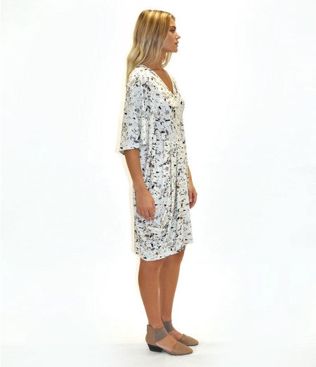 side view of blond model wearing a v-neck kaftan style dress in a white terrazzo print and taupe shoes. Against a White background