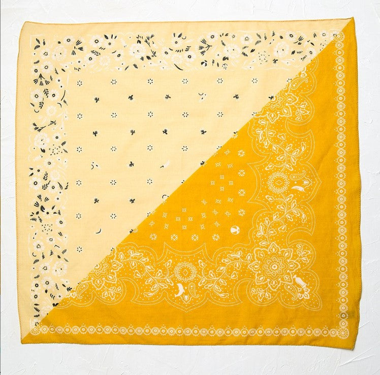 Close up of a flat sqaure bandana in a yellow and mustard color scheme with black floral print. Against a white background