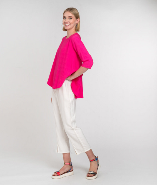 model in a hot pink top with a high-low hem, worn with a slim white pant