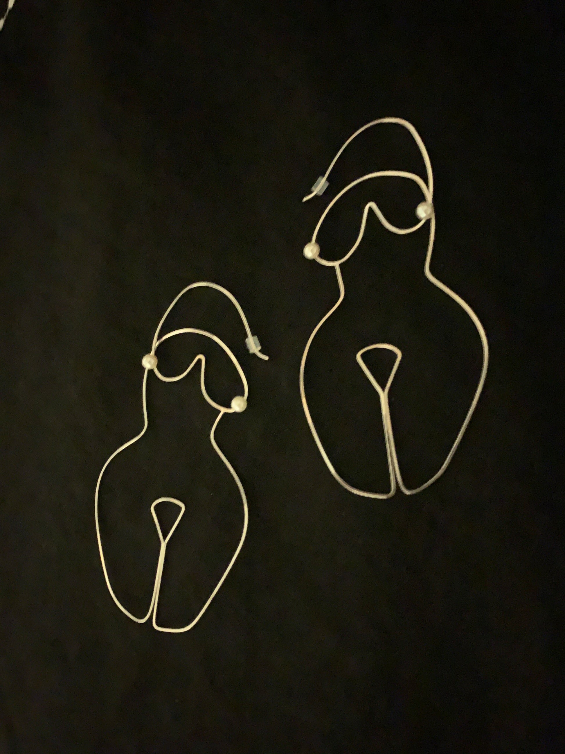 Sterling Silver wire shaped earrings formed into the shape of a woman's body with pearls as the nipples on a black background.