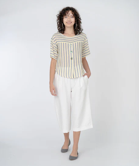 brunette model wearing yellow and black stripe crop top and white crop pants and grey flats. On a white background