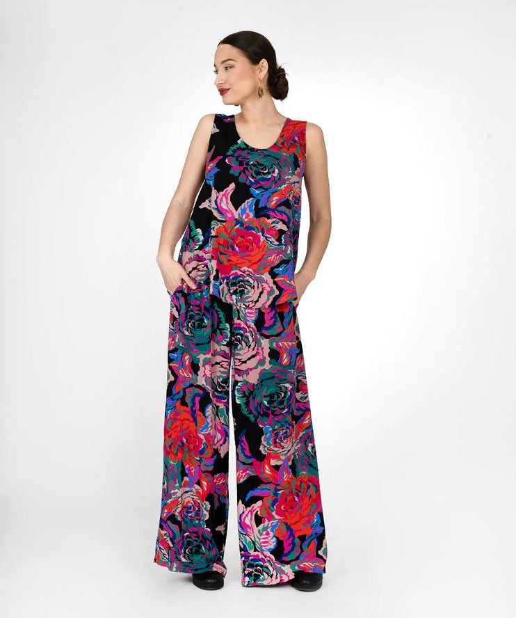 model wering a sleeveless top and full wide eg pants in a floral print with black background and bright flowrs in organce, light pink, blue and green