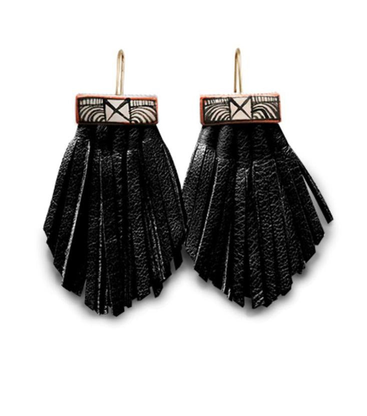 Pictured against a white background are earrings with gold wire hooks, rectangle shaped ceramic bases painted with white and black stripes, and long leather tassels that are hand cut and black.