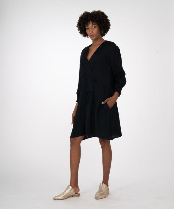 modelwearing long sleeve black knee length dress and gold mules. On a white background